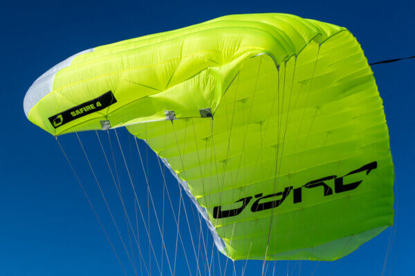 Close-up of a lime green Safire 4 skydiving canopy in flight against a blue sky.