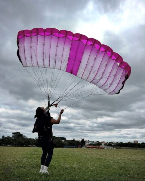 artina gathering her pink canopy on the ground after landing under cloudy skies.