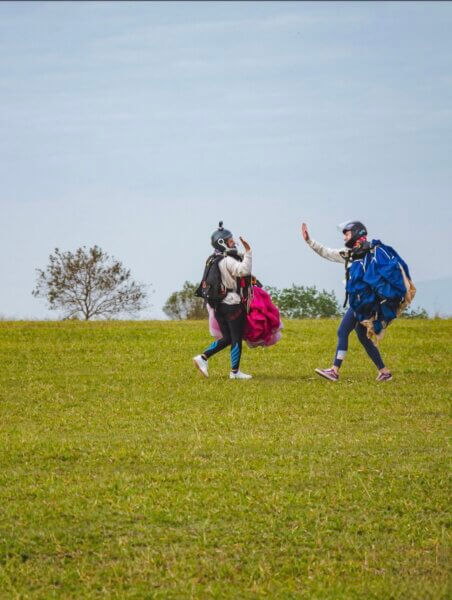 Two GO GIRLS pilots hi fi, walking back across the field after landing, canopies in tow.